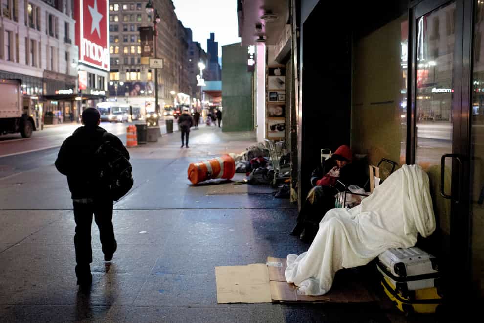 A homeless person sleeps under a blanket while seated on a New York pavement (AP)