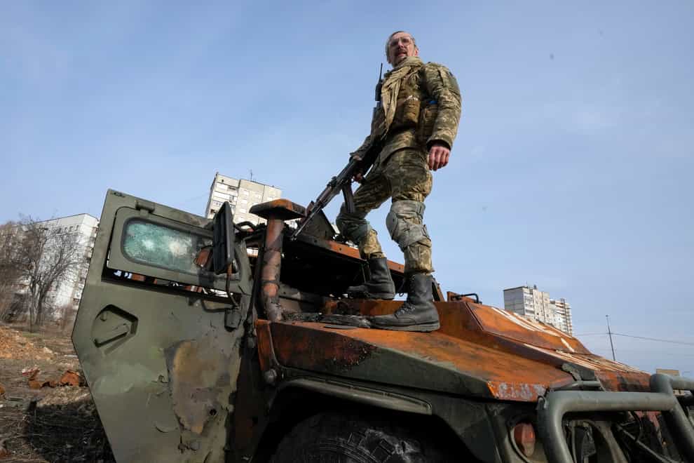A Ukrainian soldier stands on top of a destroyed Russian APC after recent battle in Kharkiv, Ukraine, Saturday, March 26, 2022 (Efrem Lukatsky/AP/PA)