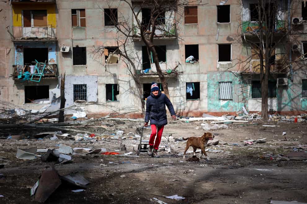 A man walks with his dog near an apartment building damaged by shelling from fighting on the outskirts of Mariupol, Ukraine, in territory under control of the separatist government of the Donetsk People’s Republic, on Tuesday, March 29, 2022. (AP Photo/Alexei Alexandrov)