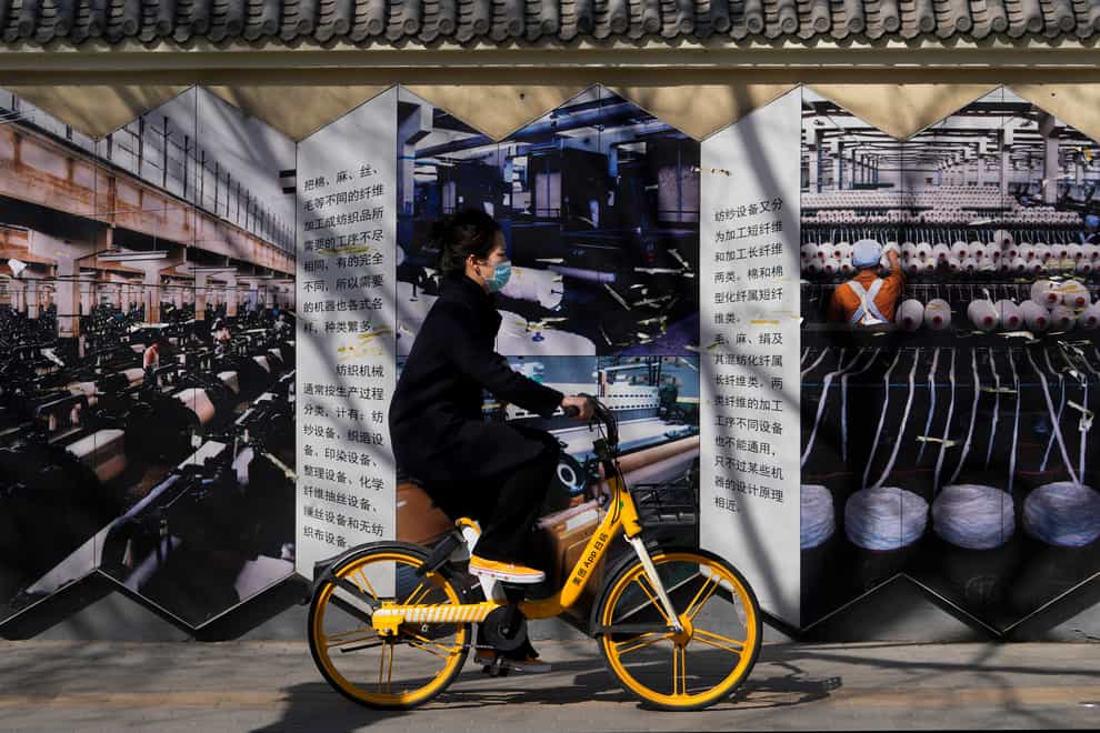 A woman rides on a bicycle past a poster depicting manufacturing industries (AP)