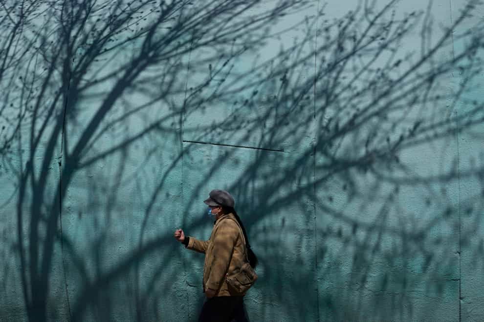 A resident wearing a mask walks past shadows of a tree in a park in Beijing (Ng Han Guan/AP)