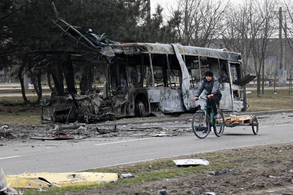 A woman rides a bicycle past a burned bus after fighting on the outskirts of Mariupol, Ukraine, in territory under control of the separatist government of the Donetsk People’s Republic, on Tuesday, March 29, 2022. (AP Photo/Alexei Alexandrov)