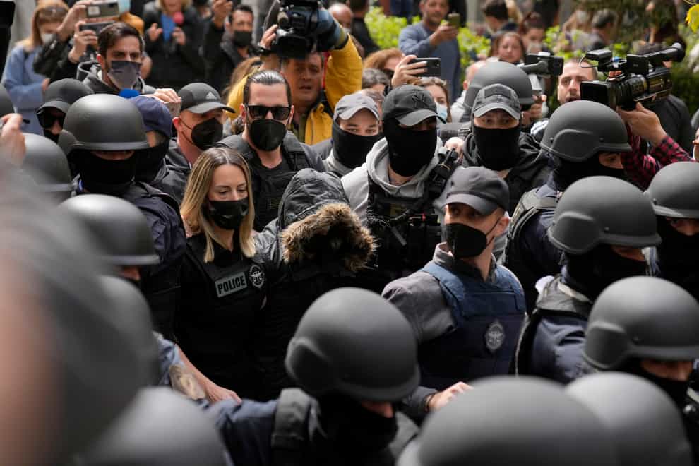 A 33-year-old woman, centre, with the hood of her coat up and wearing a protective vest, escorted by police, arrives to appear at the court in Athens, Greece, on Monday April 4 2022 (Thanassis Stavrakis/AP)