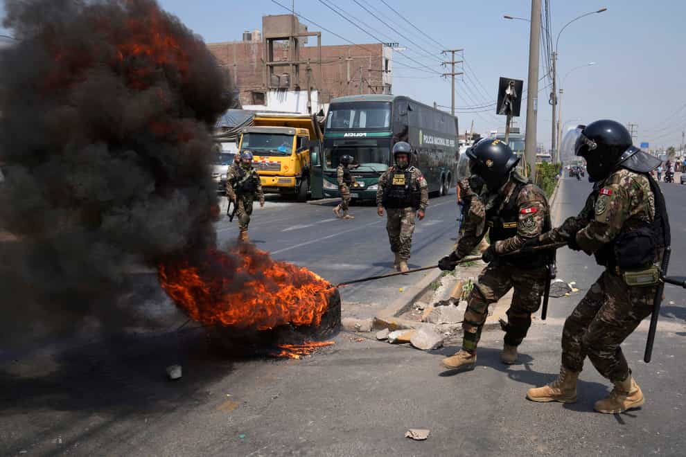 Police remove burning tires from the Central Highway where trucks and buses are parked to block the road in Huaycan on the outskirts of Lima, Peru, Monday, April 4, 2022. Cargo truckers and passenger bus drivers are blocking access to the capital to demand lower fuel prices amid inflation. (AP Photo/Martin Mejia)