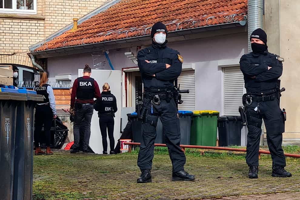 Police officers stand in front of a back entrance of a building they are searching in Eisenach, Germany, on Wednesday April 6 2022 (Martin Wichmann TV/dpa/AP)
