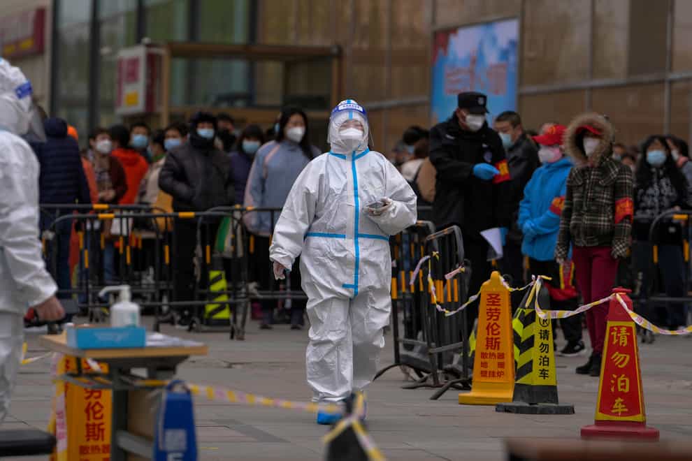 A health worker wearing a protective suit walks by masked residents who wait in line to get their throat swab at a coronavirus testing site in Beijing (Andy Wong/AP)