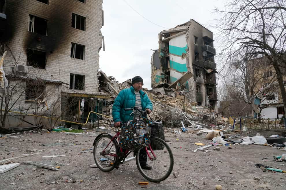 A man carries his belongings on a bike as he leaves his ruined house, background, ruined house in Borodyanka, Ukraine, on Wednesday April 6 2022 (Efrem Lukatsky/AP)