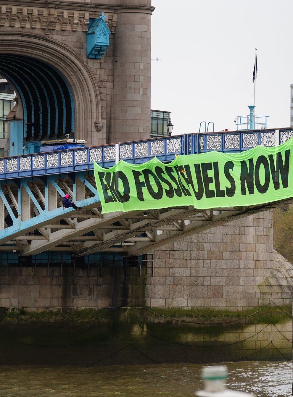Activists from Extinction Rebellion hang from Tower Bridge on suspension cords beside a giant banner that reads ‘End fossil fuels now’ (Victoria Jones/PA)