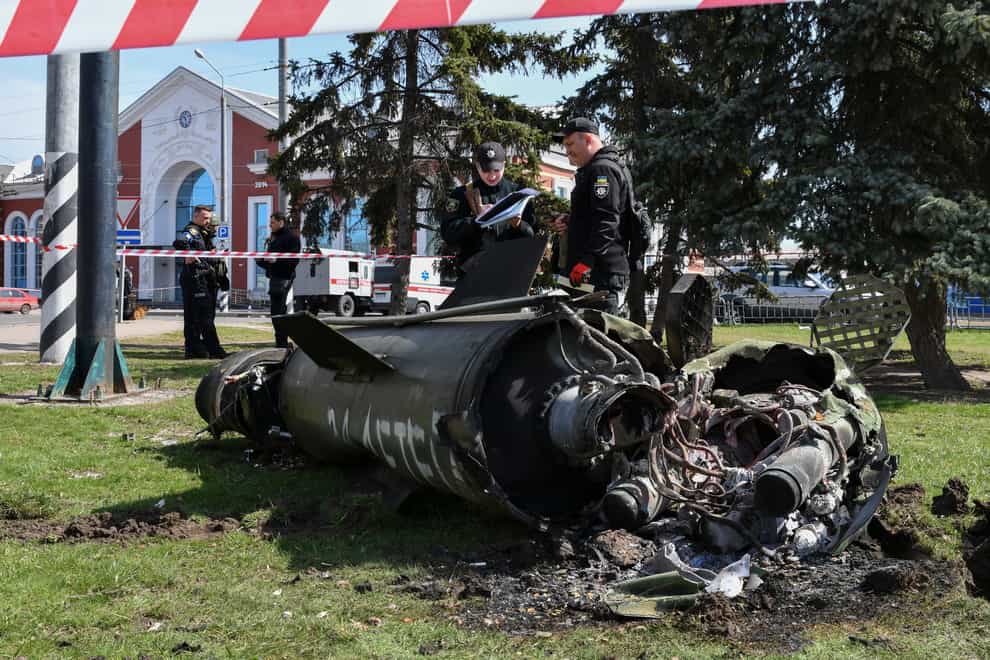 Ukrainian servicemen stand next to a fragment of a Tochka-U missile with a writing in Russian “For children” , on a grass after Russian shelling at the railway station in Kramatorsk, Ukraine, Friday, April 8, 2022. (AP Photo/Andriy Andriyenko)