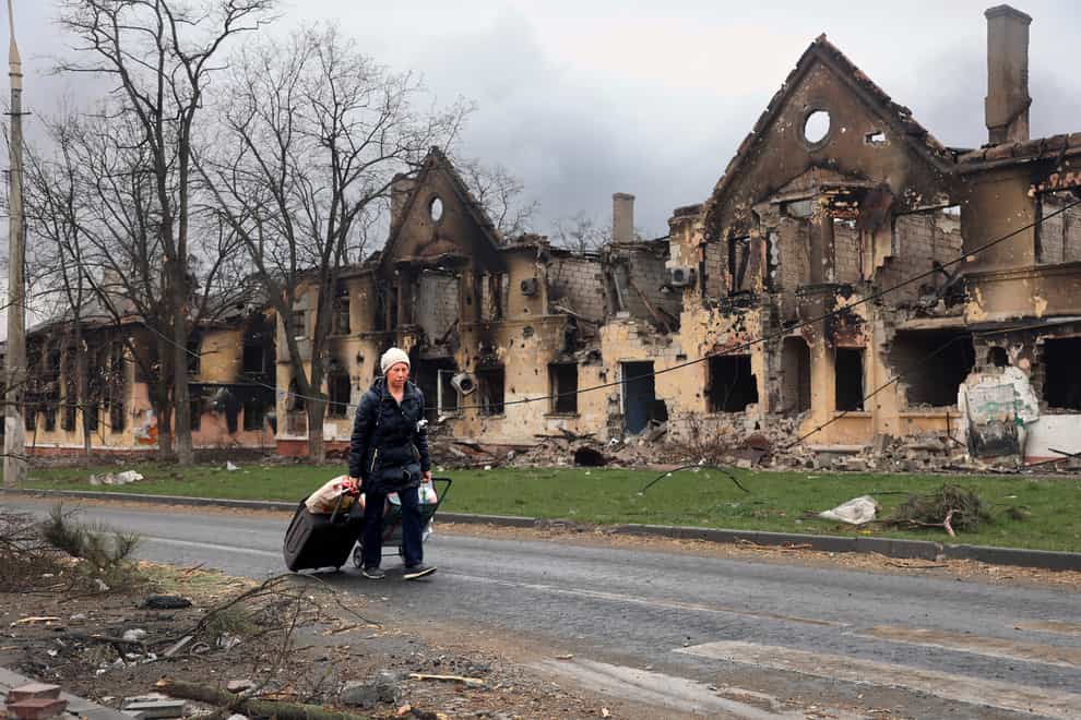 A woman pulls her bags past houses damaged during a fighting in Mariupol (Alexei Alexandrov/AP)