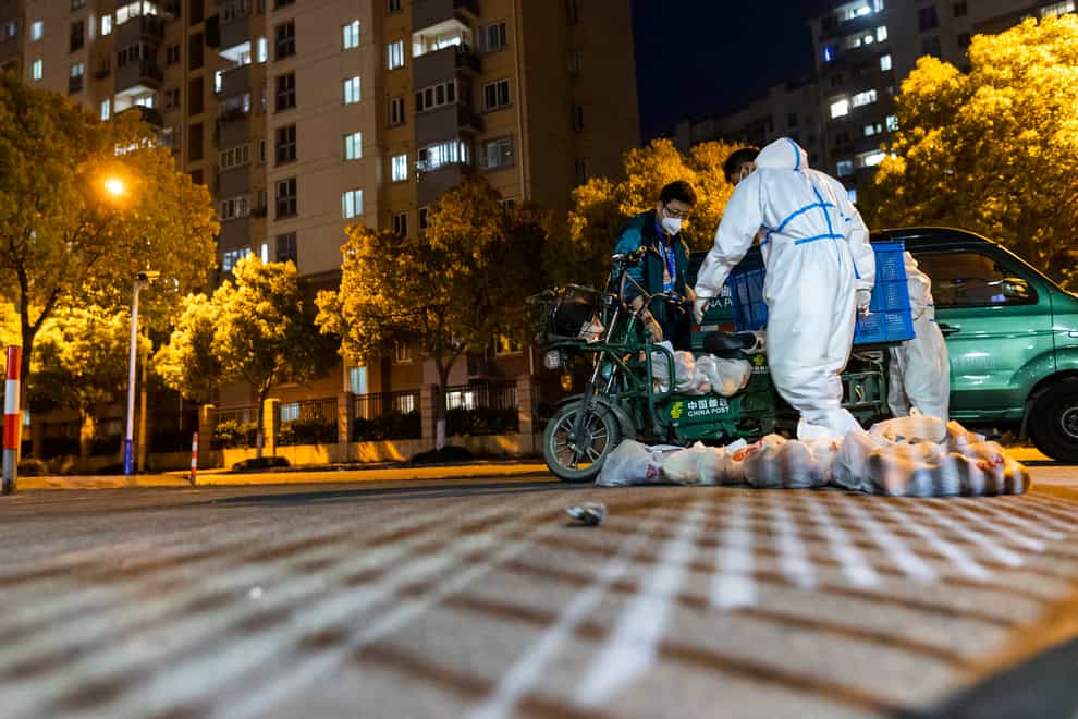 Deliverymen wearing protective suits carry bags of food at the gate of a residential community in Shanghai (AP)