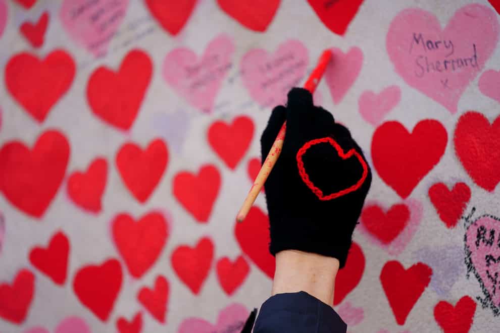 A volunteer from the Covid-19 Bereaved Families for Justice group paints a heart on the National Covid Memorial Wall opposite the Palace of Westminster in central London (Victoria Jones/PA)