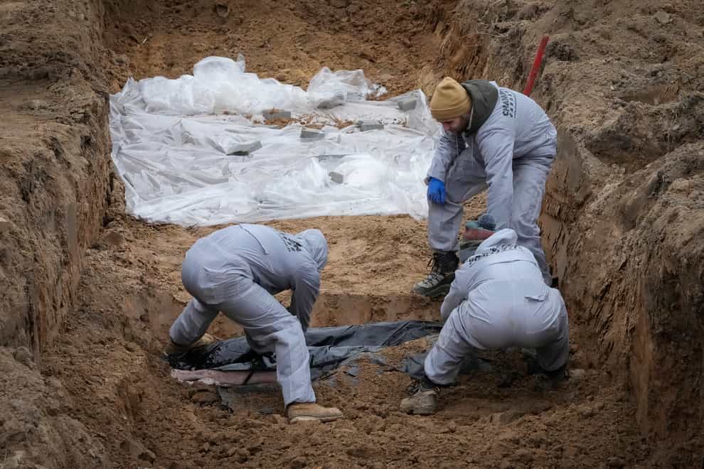 Men wearing protective gear exhume the bodies of civilians killed during the Russian occupation in Bucha (Efrem Lukatsky/AP)