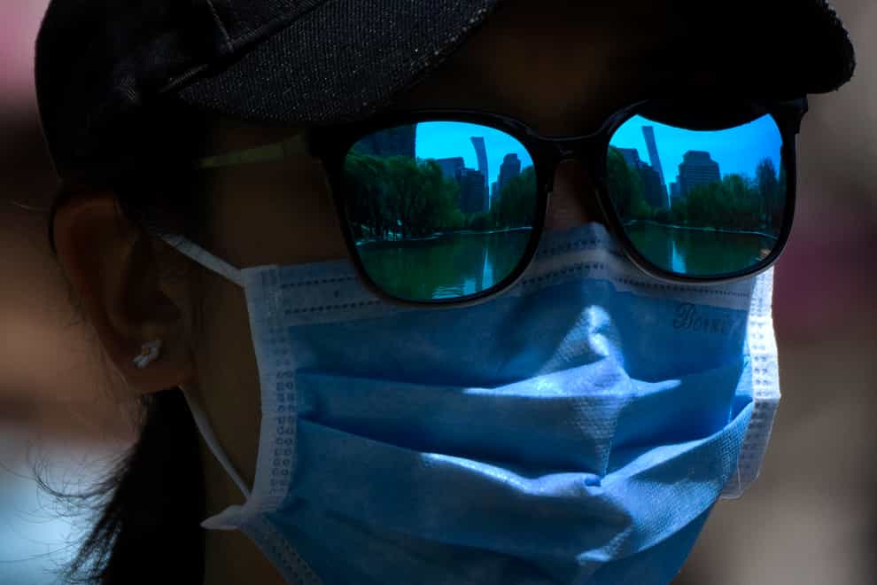 The skyline of Beijing is reflected in the sunglasses of a woman wearing a face mask (Mark Schiefelbein/AP)
