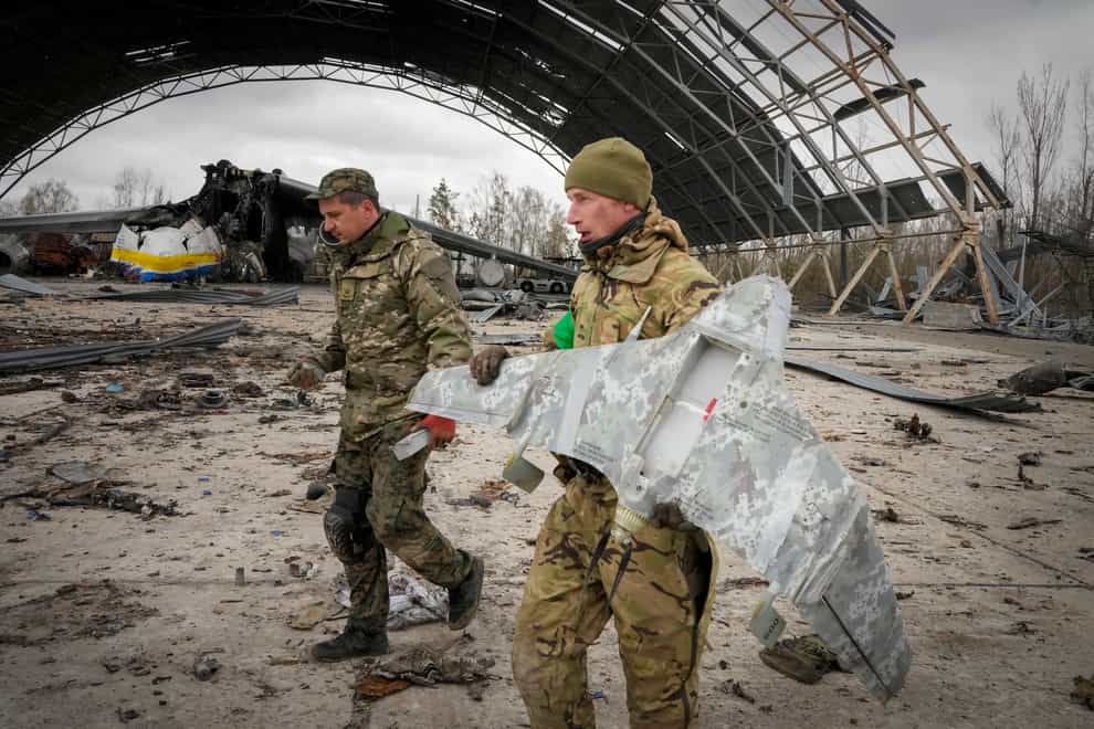 Ukrainian sappers carry a Russian military drone backdropped by the Antonov An-225, world’s biggest cargo aircraft destroyed by the Russian troops during recent fighting, at the Antonov airport in Hostomel, on the outskirts of Kyiv, Ukraine, Monday, April 18, 2022. (AP Photo/Efrem Lukatsky)