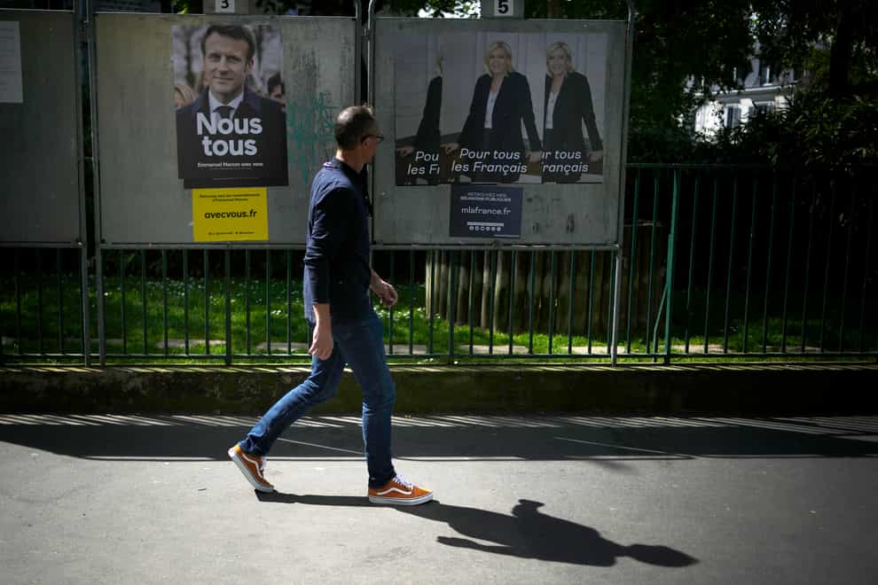 A man walks in front of campaign posters of Emmanuel Macron and Marine Le Pen (Christophe Ena/AP)