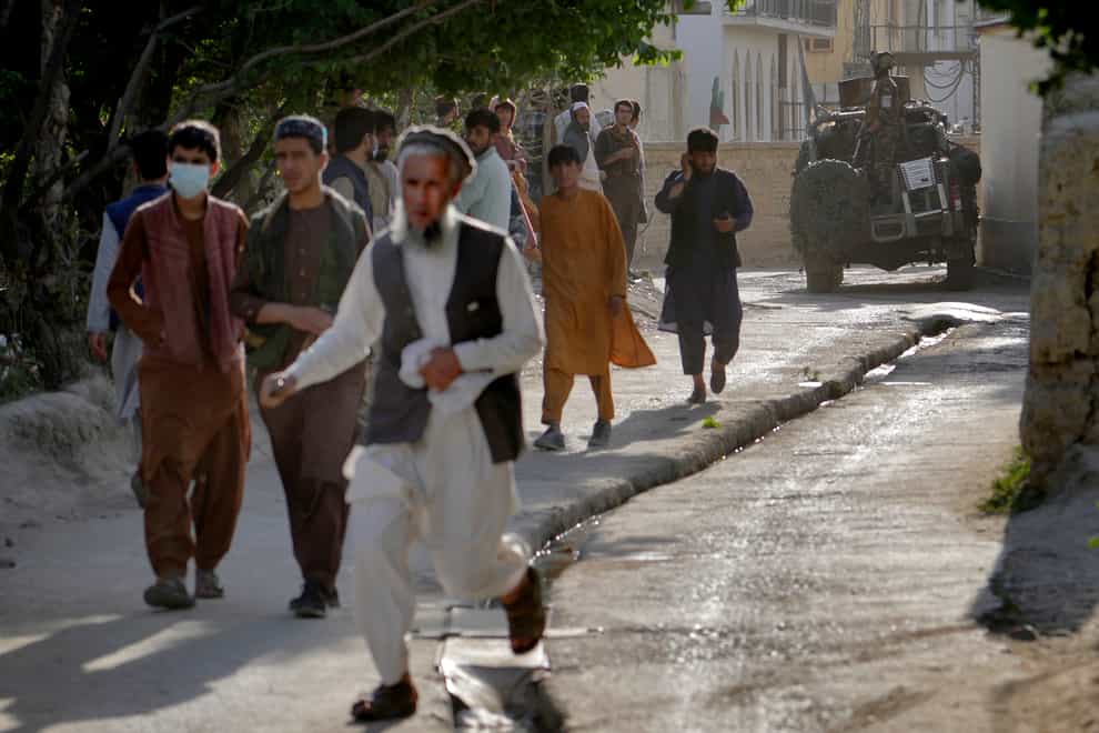People leave the site of an explosion as a Taliban fighter stands guard in Kabul, Afghanistan (Ebrahim Noroozi/AP)