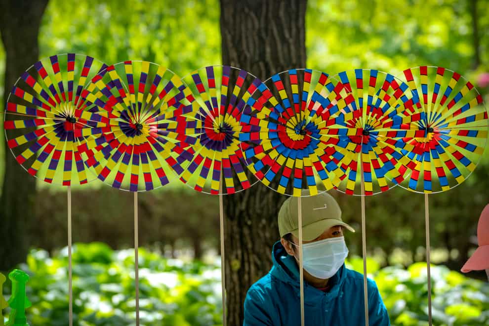 A vendor wearing a face mask sits near pinwheels for sale at a public park in Beijing (Mark Schiefelbein/AP)