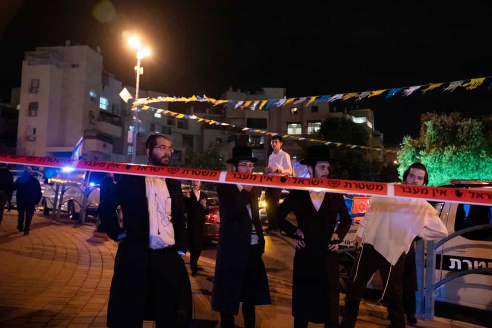 Ultra-Orthodox Jews stand behind police tape after a stabbing attack in the town of Elad (AP)