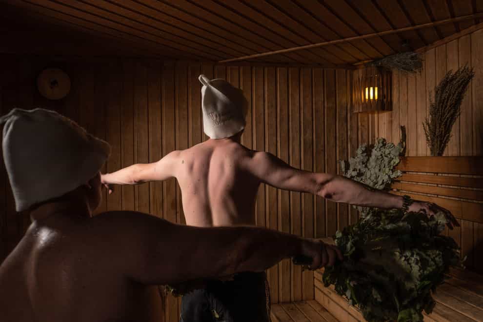 A bather massages a man with a broom of oak and birch in a wooden sauna (Alamy/PA)