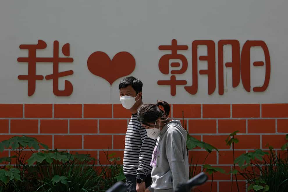 A couple wearing face masks walk by a wall displaying a words “I Love Chaoyang” as they heading to get tested for Covid-19 in the Chaoyang district in Beijing (Andy Wong/AP)