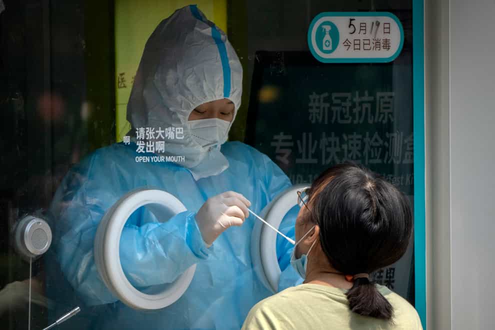 A worker wearing a protective suit administers a Covid-19 test at a coronavirus testing site in Beijing (Mark Schiefelbein/AP)