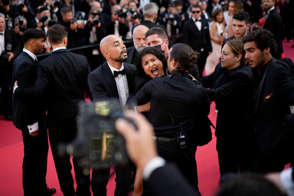 A protester wearing body paint that read “Stop Raping Us” is removed from the red carpet (Daniel Cole/AP)