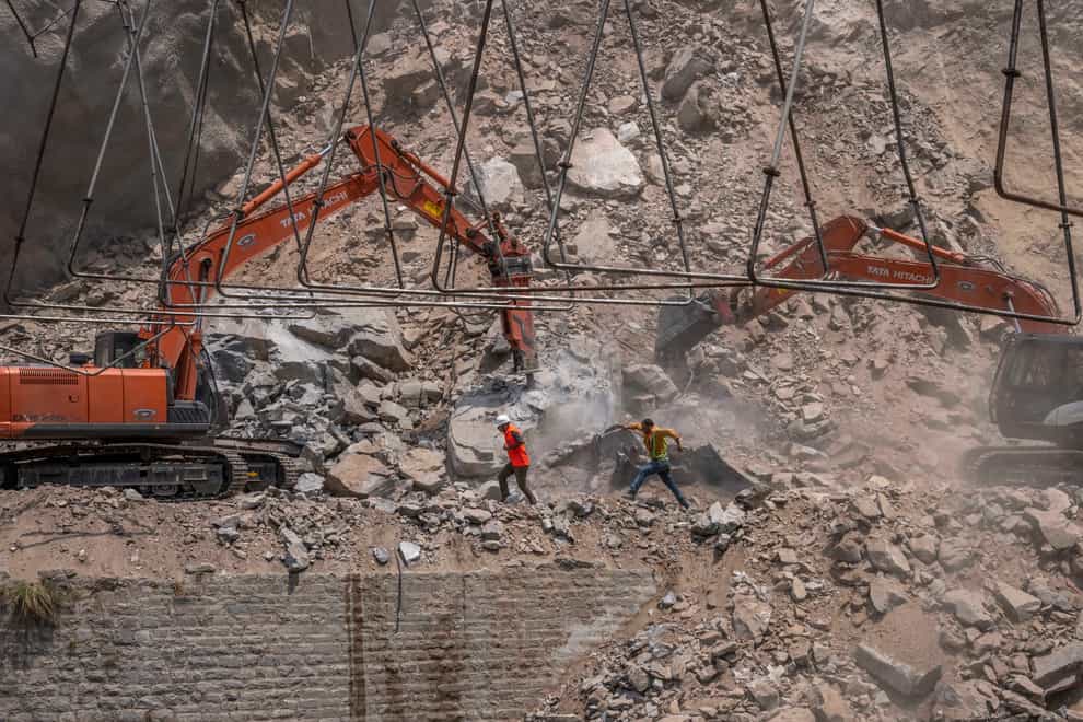 Rescue workers run for cover as earth movers dig through rubble of a collapsed tunnel in Ramban district, south of Srinagar, Indian controlled Kashmir, on Friday May 20 2022 (Dar Yasin/AP)