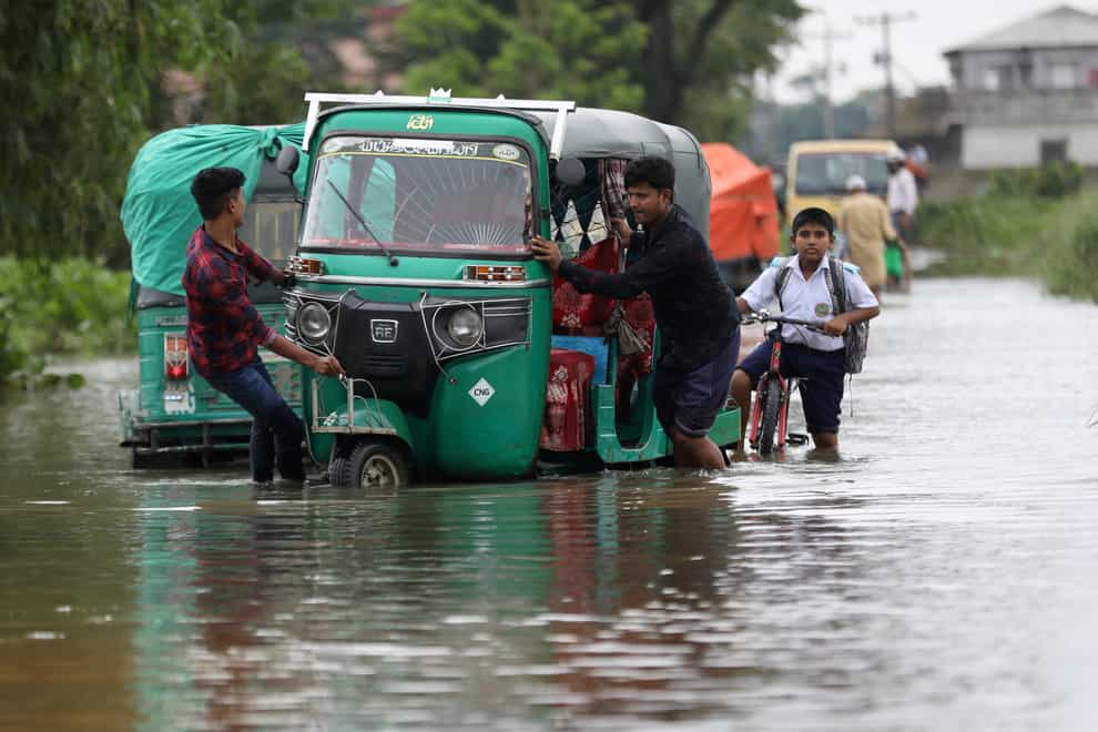 People push an auto rickshaw through a flooded road as a school boy rides his bicycle behind in the Bagha area in Sylhet, Bangladesh, on Monday May 23 2022 (AP)