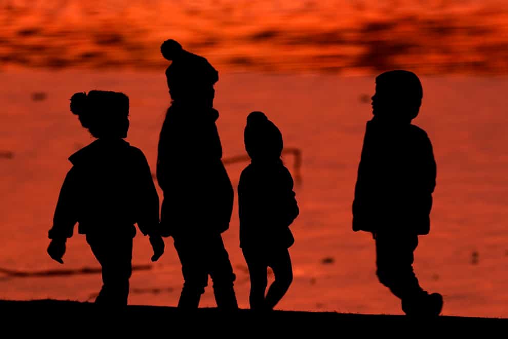 Children are silhouetted against a pond at a park (Charlie Riedel/AP)