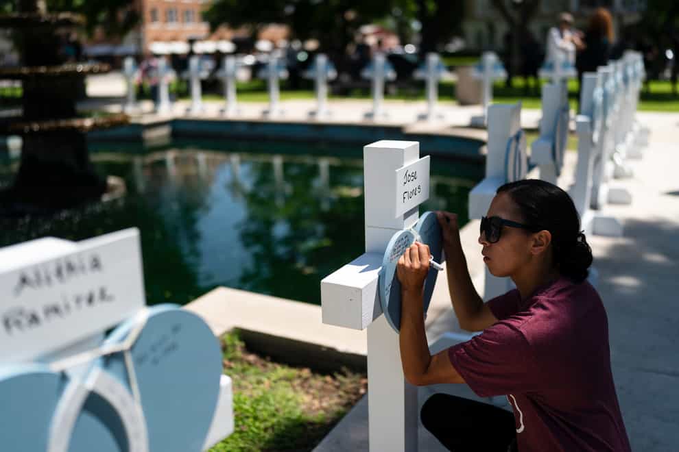 A women writes a message on a memorial cross for Jose Flores, one of the Robb Elementary School shooting victims (Jae C. Hong/AP)