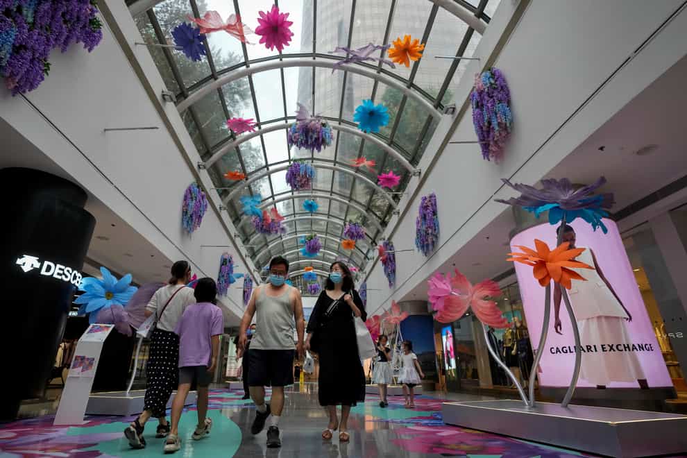 Residents wearing face masks walk through a reopened shopping mall decorated with colourful flowers in Beijing (Andy Wong/AP)
