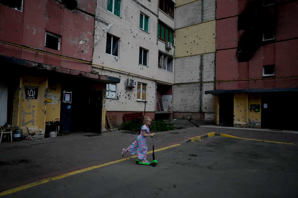A girl rides a scooter near buildings destroyed during attacks in Irpin, on the outskirts of Kyiv, Ukraine (Natacha Pisarenko/AP)