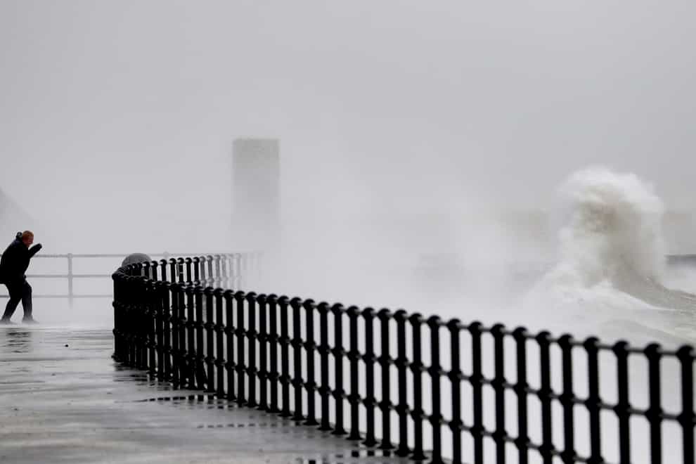 A man watches waves crashing over the promenade (Gareth Fuller/PA)