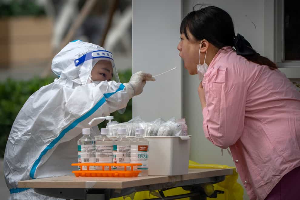 A worker wearing a protective suit swabs a woman’s throat for a Covid-19 test at a coronavirus testing site in Beijing (Mark Schiefelbein/AP)