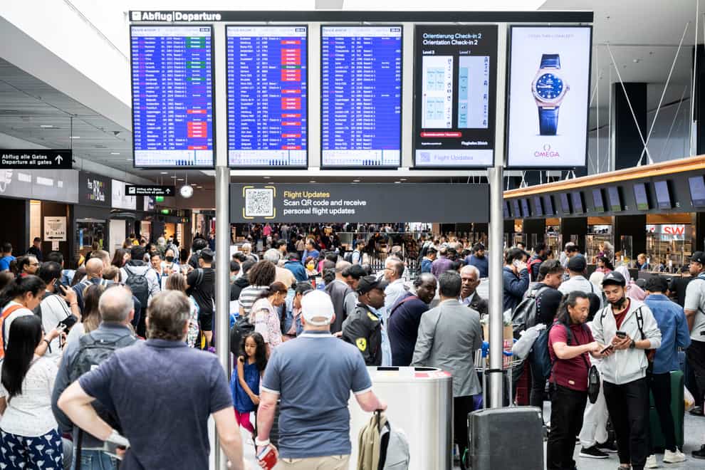 Passengers wait in front of a display board at Zurich airport, in Zurich, on Wednesday June 15 2022 (Ennio Leanza/Keystone/AP)