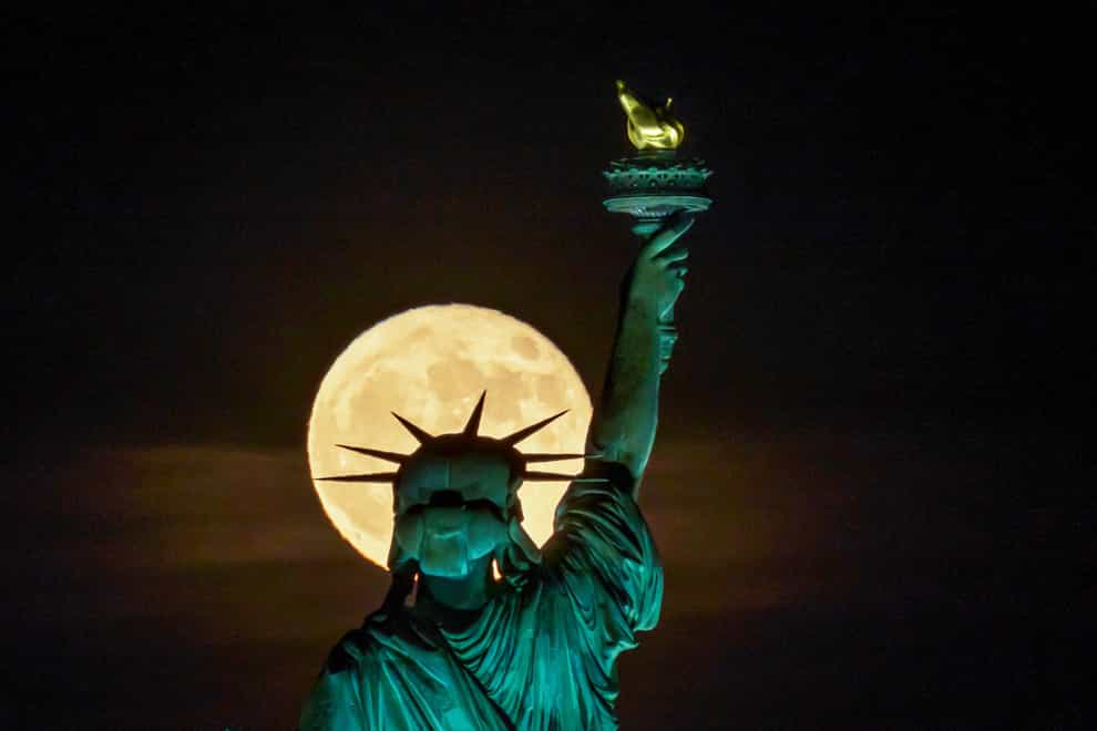 The Strawberry Supermoon rises in front of the Statue of Liberty in New York (J. David Ake/AP)