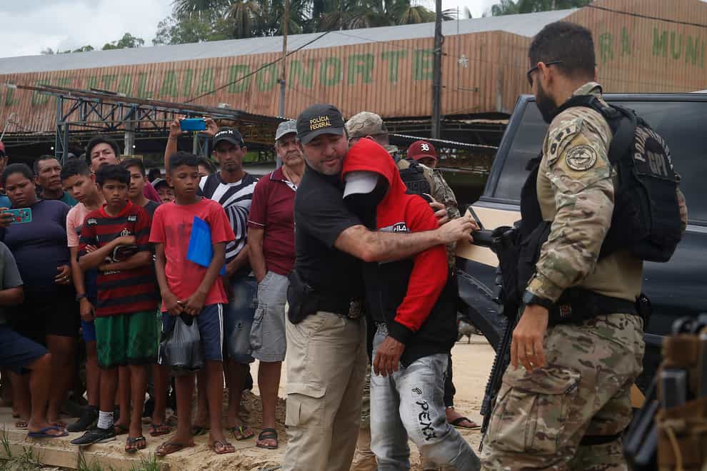 A federal police officer escorts a suspect towards a river in the area where Indigenous expert Bruno Pereira and freelance British journalist Dom Phillips disappeared (Edmar Barros/AP)