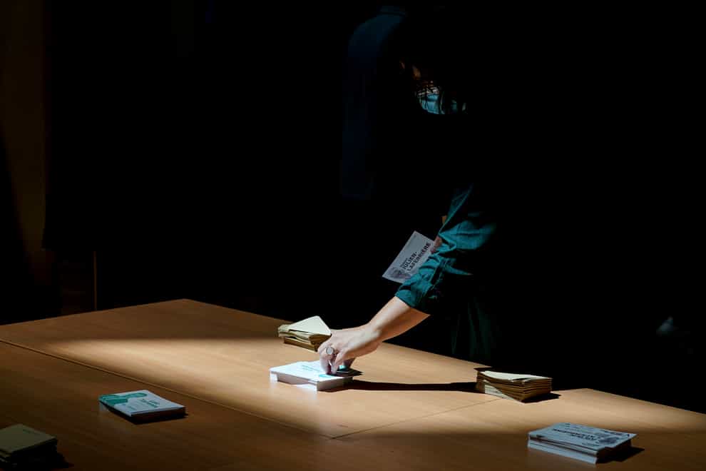 A voter picks up ballots before voting in the second round of the French parliamentary election in Lyon, central France (Laurent Cipriani/AP)
