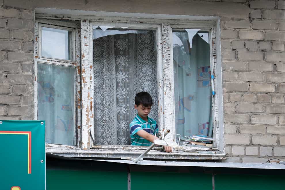 A boy removes broken glass from a window’s frame after shelling in Donetsk (Alexei Alexandrov/AP)