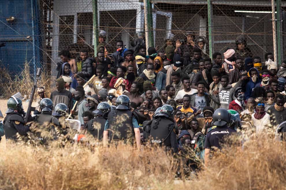 Riot police stand guard in front of a group of migrants at the Spanish border in Morocco (Javier Bernardo/AP)