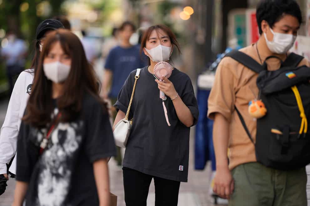 A woman uses a portable electric fan while strolling down the street with her friends in Tokyo (AP)
