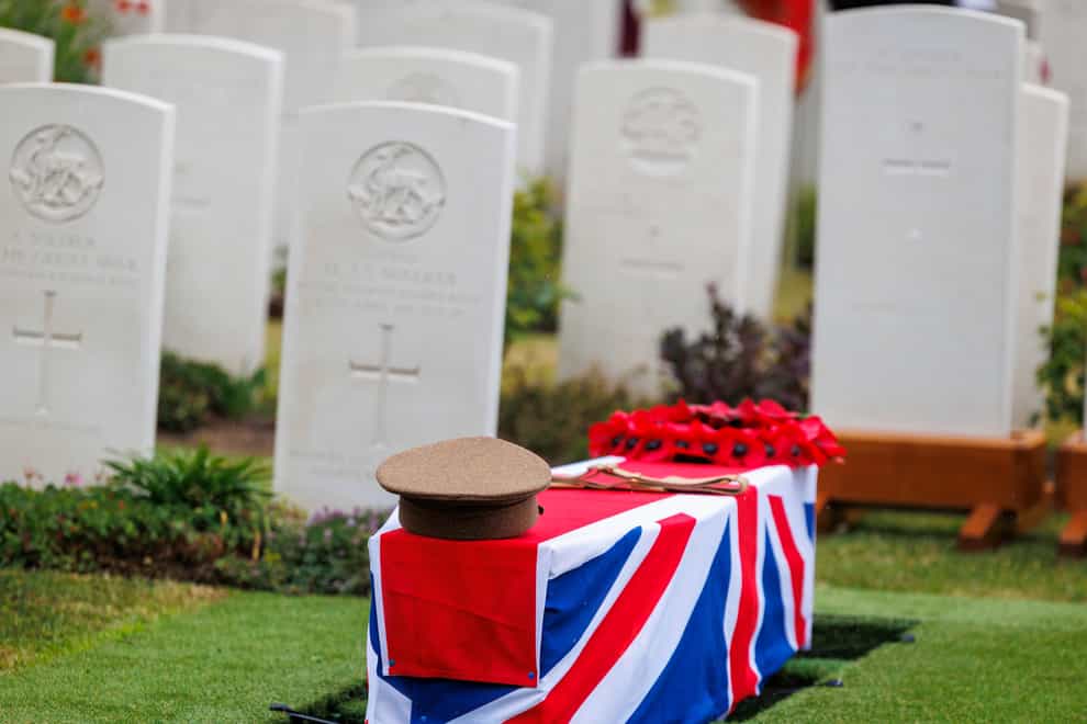 A regimental hat and a poppy wreath are placed on the coffin of an unidentified British soldier (Olivier Matthys/AP)