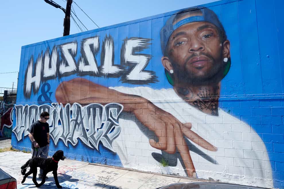 A man walks his dog past a street mural of the late rapper Nipsey Hussle in Los Angeles (Chris Pizzello/AP)