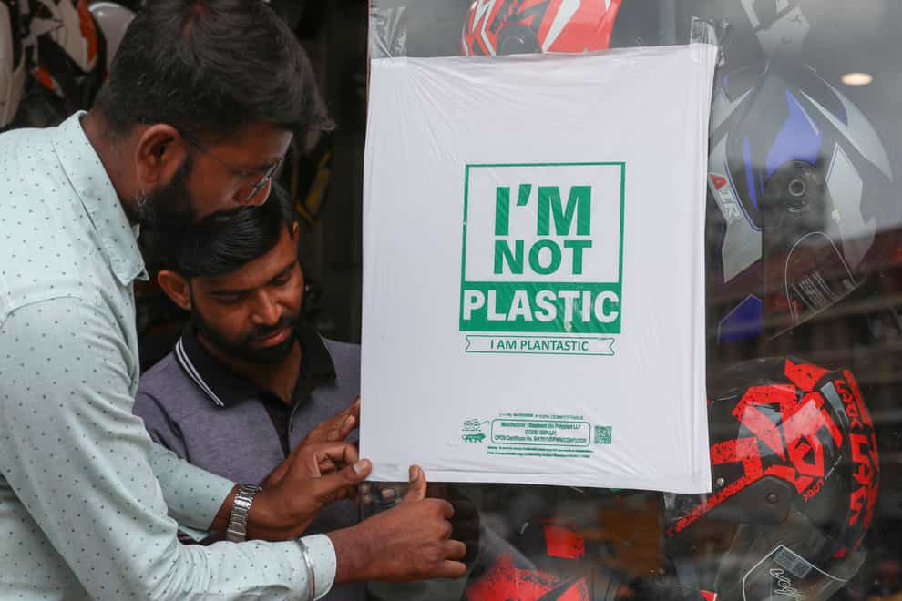 Workers of a helmet store paste degradable plastic substitute material on a glass in Hyderabad (Mahesh Kumar A/AP)