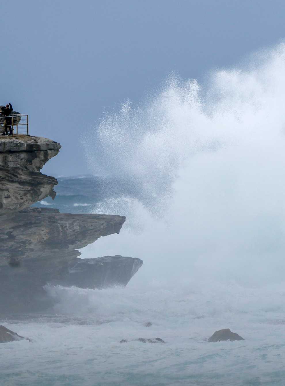 People stand on a rock ledge as huge swells hit the headland at Bondi Beach in Sydney, Australia (Mark Baker/AP)