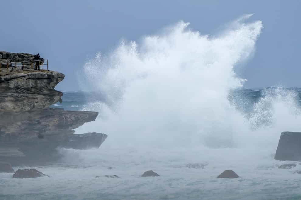 People stand on a rock ledge as huge swells hit the headland at Bondi Beach in Sydney, Australia (Mark Baker/AP)