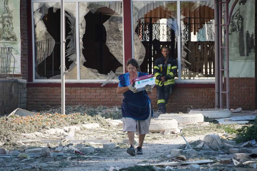 A cleaner takes out the surviving paper for the printer from a school destroyed during a missile strike in Kharkiv (AP)