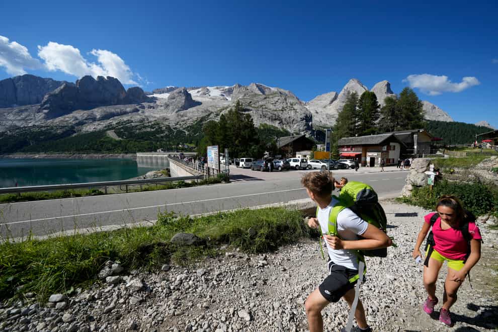Hikers walk past the Marmolada mountain and the Punta Rocca glacier near Canazei, in the Italian Alps in northern Italy (Luca Bruno/AP)
