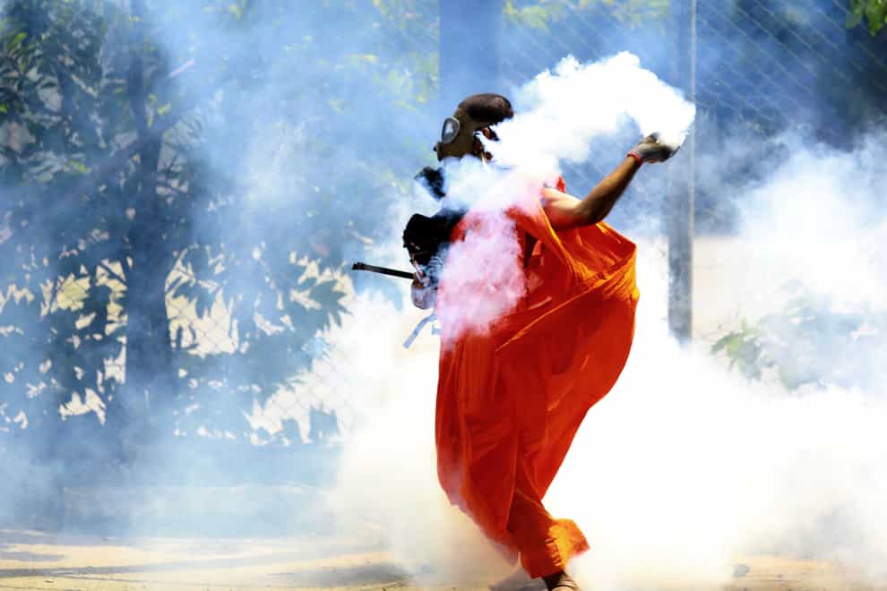 A man throws back a tear gas canister after it was fired by police to disperse protesters in Colombo (AP)